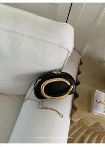 Mini black round evening bag featuring a striking gold C-shaped metal handle and chain strap.