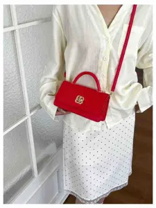Dettaglio borsa a spalla rossa con elegante serratura a trifoglio e materiale in ecopelle liscia.
