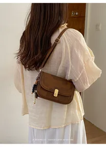 Sac bandoulière rétro marron sous les bras avec serrage métal et perles, détail mode.