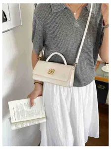 Vista dettagliata dell'elegante borsa a baguette bianca con chiusura floreale dorata.