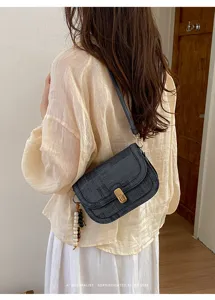 Gros plan sur un sac à épaule vintage à imprimé journal, fermoir doré et pendentif perlé.