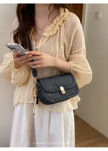 Gros plan du sac bandoulière rétro noir avec serrure dorée et charm perlé en situation réelle.