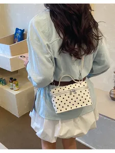 Detail view of stylish white polka dot crossbody vanity bag with top handle and zipper.