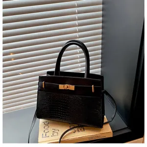 Detailed view of a black top-handle crossbody bag with crocodile texture and metal turn-lock.