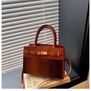Detail view of stylish brown crocodile texture handbag with metal turn lock and strap.