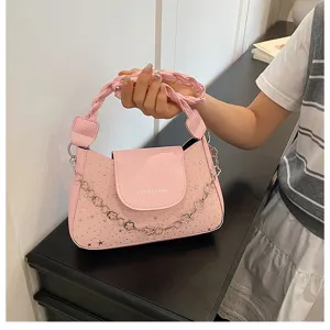 Dettaglio borsa a spalla rosa con borchie a stella, manico intrecciato e catena in metallo.
