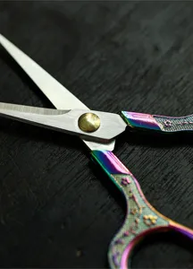 Close-up of vintage iridescent titanium tea scissors with plum blossom handle details on dark wood.