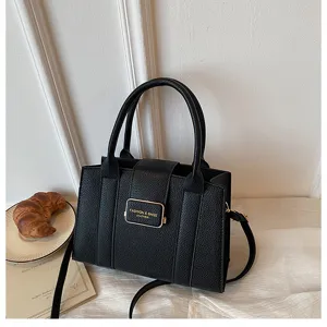 Détail d'un sac à bandoulière en cuir noir, doté de deux poignées et d'un fermoir en métal.