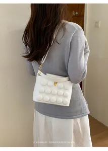 Elegante borsa a tracolla bianca con motivo a bolle e fibbia a V dorata per stile chic.