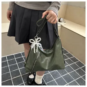 Détail du sac à épaule vert foncé en cuir avec poche avant et pendentif nœud perlé.