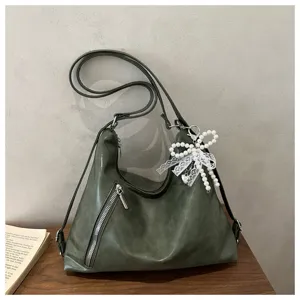 Détail de sac porté épaule besace vert foncé avec charmant nœud en perles et fermeture éclair avant.