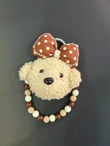 Détail du porte-clés chien en peluche avec nœud à pois marron et bracelet en perles.