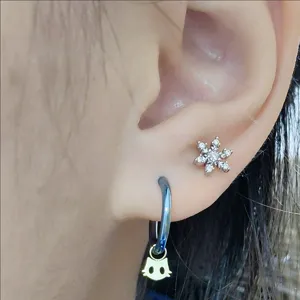 Close-up detail shot of titanium cartilage stud with sparkling zircon and cute cat hoop earring.