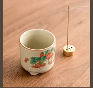 Vista dettagliata del bruciaincenso in ceramica con fragole e supporto su legno.
