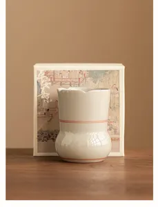 Nahaufnahme eines handgefertigten Keramik-Teezubehörs mit feinem roten Linien-Design auf Holztisch.