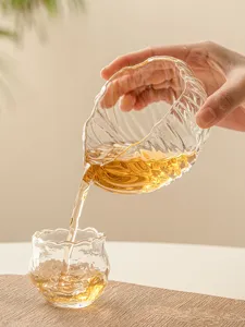 Clear glass tea pitcher detail showing golden tea pouring into a cup, heat-resistant.