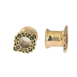 Nahaufnahme Detail von goldenem Ohrtunnel Piercing Schmuck mit feinem schwarzen Blumenmuster.