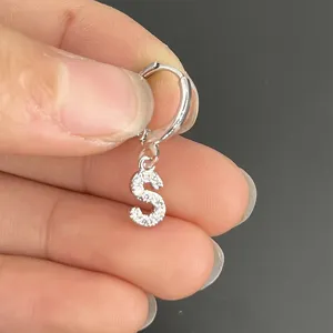 Detailopname van een zilveren oorring met letter S hanger en schitterende zirkoniastenen.