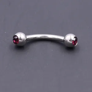 Stainless steel curved eyebrow barbell featuring red crystal ends, detailed closeup view.