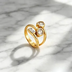 Nahaufnahme eines asymmetrischen, vergoldeten Edelstahlrings mit funkelnden Kristallsteinen.