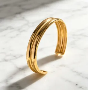 Dettaglio di un elegante bracciale rigido doppio in acciaio placcato oro su marmo.