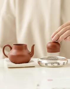 Vue détaillée d'une théière traditionnelle en argile et repose-couvercle argenté avec finesse.
