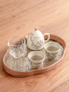 Detalle del juego de té de magnolia pintado a mano con tetera de cerámica en bandeja de madera.