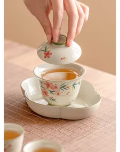 Gros plan sur les détails de la tasse à thé gaiwan en céramique à fleurs de pêcher peintes.
