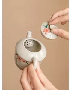 Detalle de tetera de cerámica pintada a mano con tapa y filtro de bola para viaje y té.