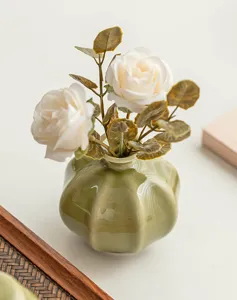 Close-up detail of the green ceramic vase with artificial white roses for desktop decor.
