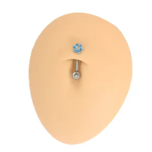 Primo piano dettagliato di un piercing per ombelico con fiore blu su modello in silicone.