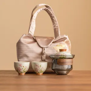 Service à thé de voyage en céramique avec théière en verre, deux tasses et sac élégant.