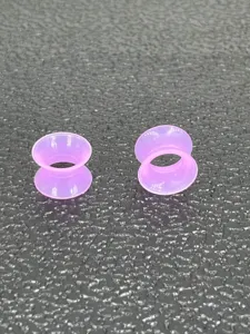 Close-up detail of soft pink silicone double flared ear tunnels for body piercing jewelry.