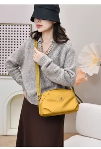 Detail shot of the yellow nylon crossbody bag, showing strap texture and metal badge accent.