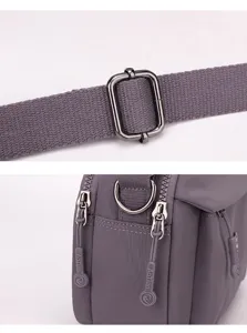 Close up detail view of grey nylon crossbody bag strap buckle and zipper puller hardware.