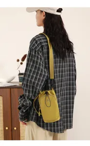Detail view of a stylish yellow crossbody bag with wide strap and secure drawstring design.