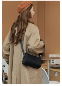 Detailed shot of stylish black cylindrical shoulder bag with branded strap in cafe setting.