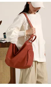 Close-up detail shot of the versatile rust red shoulder dumpling bag worn by model indoors.