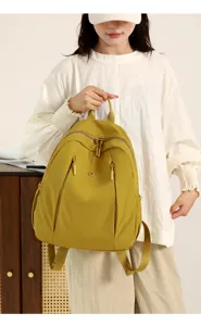 Detailed shot of yellow nylon casual backpack held by model, showing zipper and front pocket design.