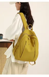 Detail shot of minimalist nylon backpack in yellow, featuring multi-zipper pockets and wide straps.