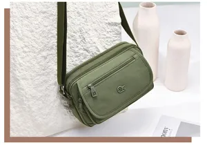 Green nylon multi-layer crossbody bag, detail view showing zipper pockets and strap.