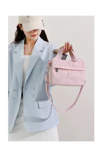 Detailed view of the pink nylon shoulder bag held by a model, featuring multi-compartment design.