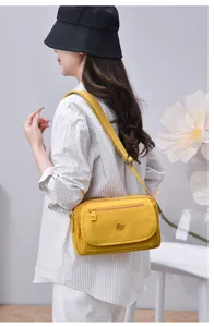 Yellow multi-layer nylon crossbody shoulder bag, detailed view of wearing and zipper pockets.