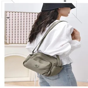 Detail view of the women's greyish-green crossbody shoulder bag worn by model, multi-pockets.