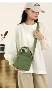 Green canvas crossbody bag detail showing front zipper pocket, handle, and shoulder strap.