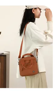 Detail view of a brown canvas shoulder crossbody bag with top handle and front zipper pocket.