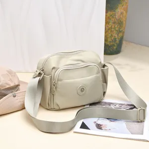 Beige nylon crossbody bag with multi-zip compartments and adjustable strap for daily use.