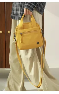 Detail view of the yellow canvas crossbody bag featuring front zipper pocket and web handles.