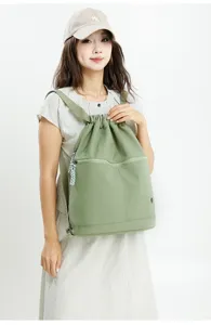 Detail shot of a green casual drawstring backpack with front zipped pocket and woven zipper pull.