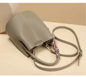 Elegant taupe leather bucket bag featuring a top handle, adjustable shoulder strap and stylish scarf.